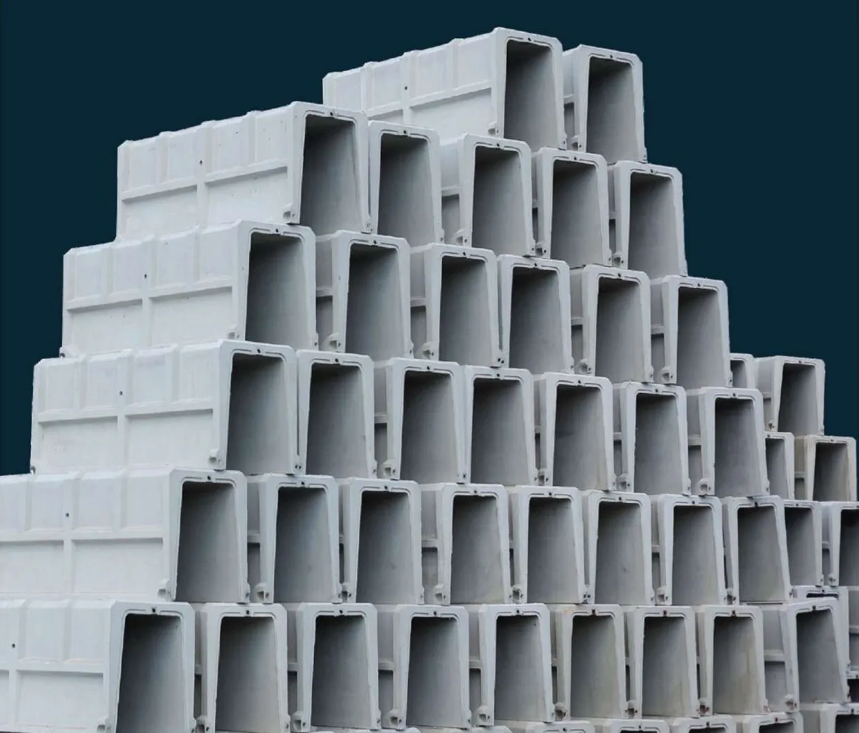 A tall stepped stack of grey precast U-shape drain units against a dark navy background