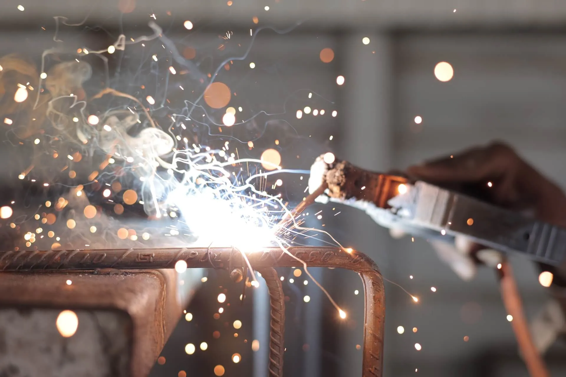 Close-up of a welder joining steel reinforcement bars, sparks flying